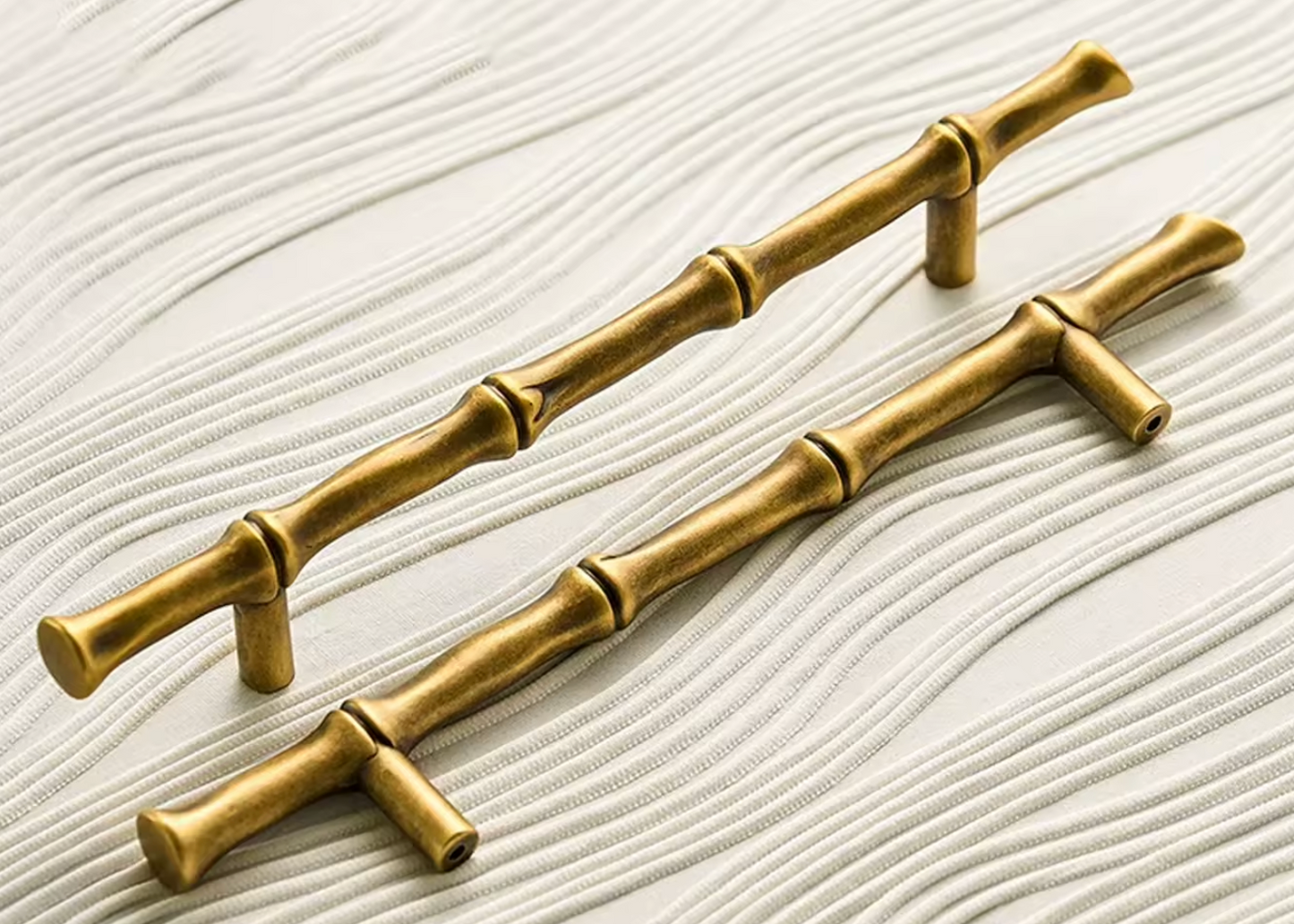 Two brass cabinet handles designed to look like bamboo stalks with natural nodes, displayed on a white textured background.