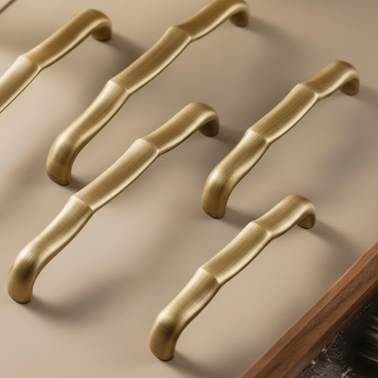 Five curved cabinet handles in a brushed gold finish arranged diagonally on a beige surface, with a dark wood trim visible in the lower right corner.