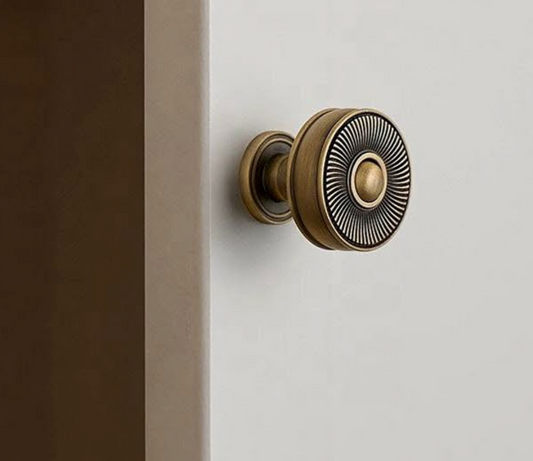 A round antique bronze door knob with a textured sunburst pattern on the face, mounted on a white door next to a dark brown door frame.