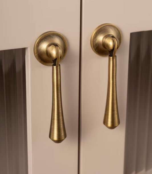 Two brass pull handles mounted on a cream-colored cabinet door, shown in a close-up view.