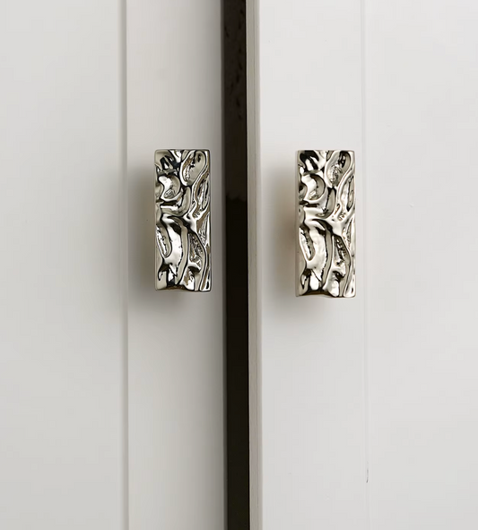 Two rectangular silver cabinet pulls with an embossed textured, organic pattern, mounted on white paneled doors.