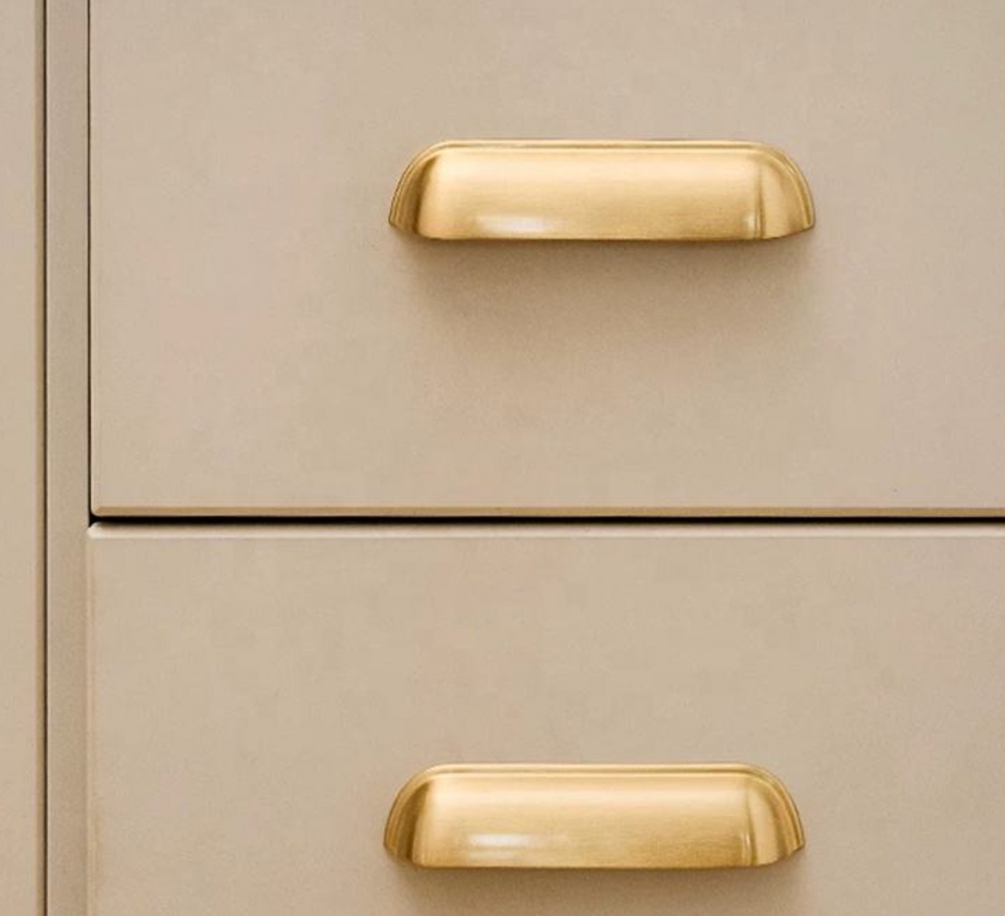 Close-up of a two-drawer cabinet with warm beige panels and polished gold pull handles.