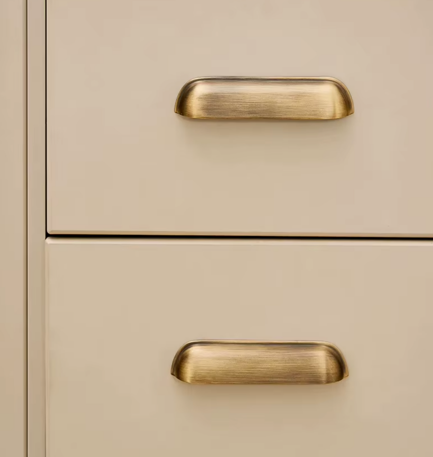 Close-up of two cream-colored drawers with matching elongated brushed brass handles.
