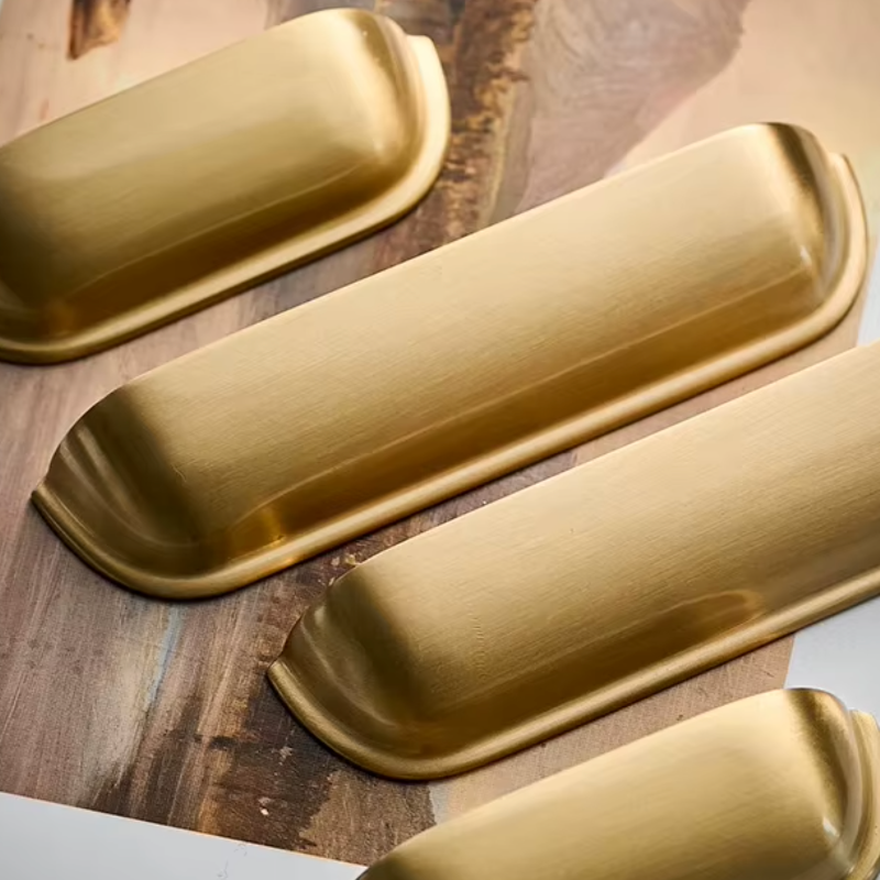 Four brushed gold cabinet knobs arranged diagonally on a rustic wooden surface.