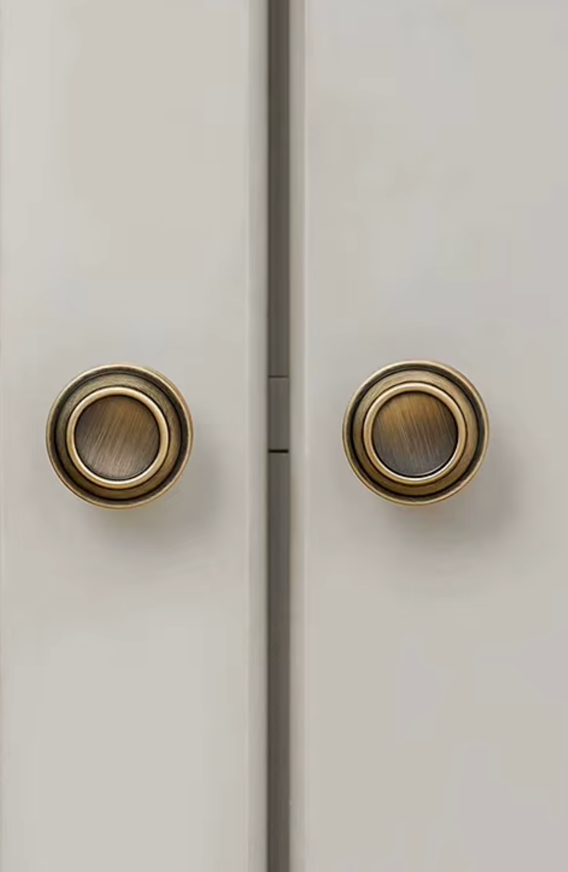 Two round antique brass door knobs mounted on light beige double doors, separated by a vertical seam.