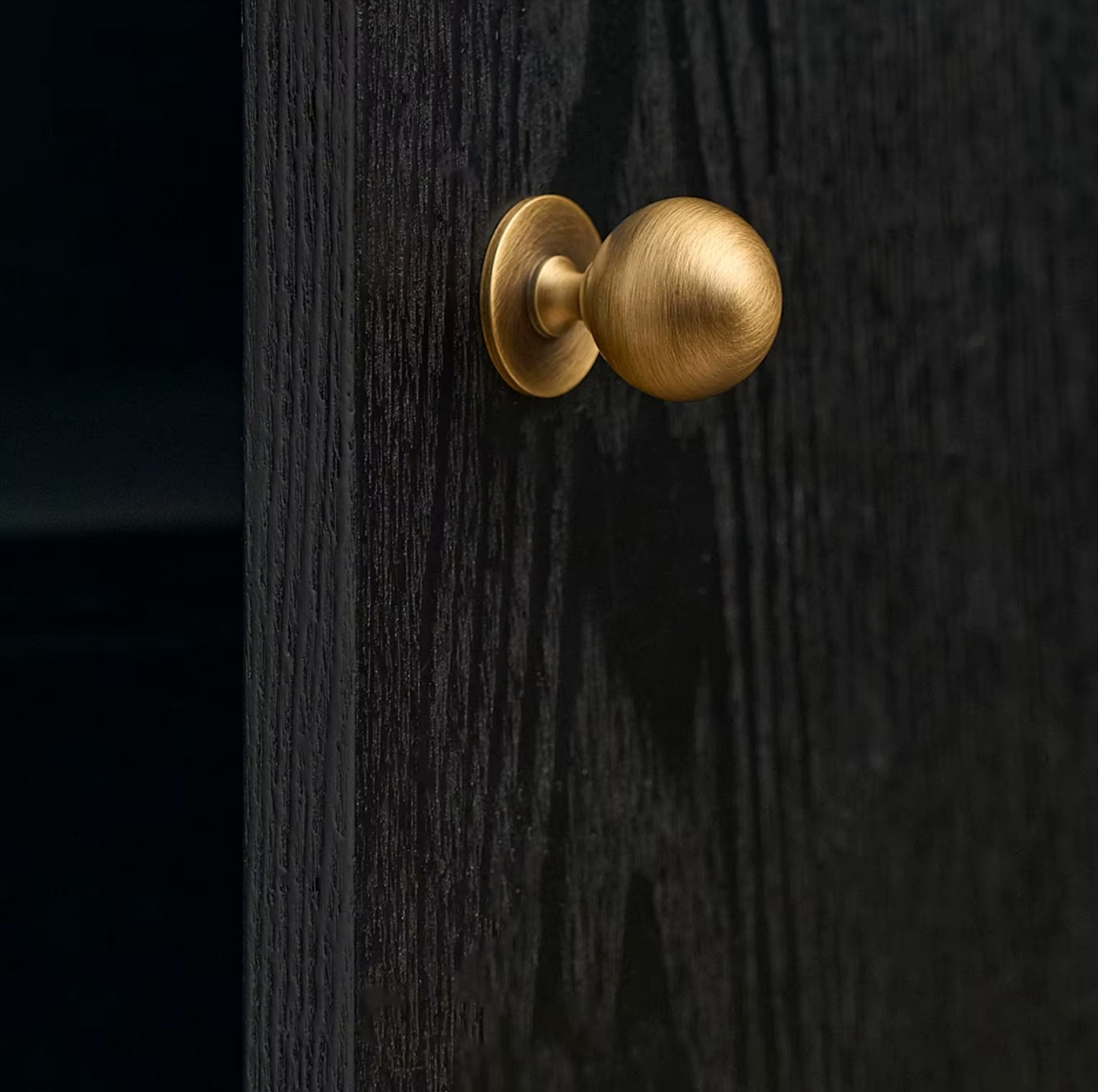 A close-up of a round brass door knob mounted on a dark wood door.