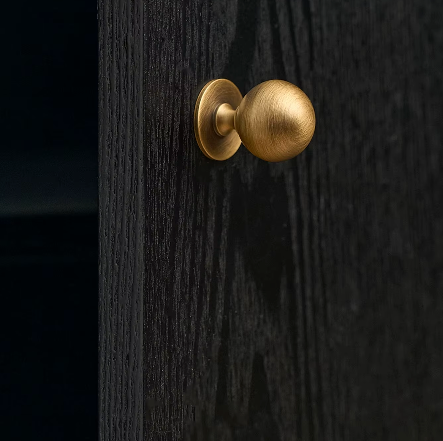 A close-up of a round brass door knob mounted on a dark wood door.