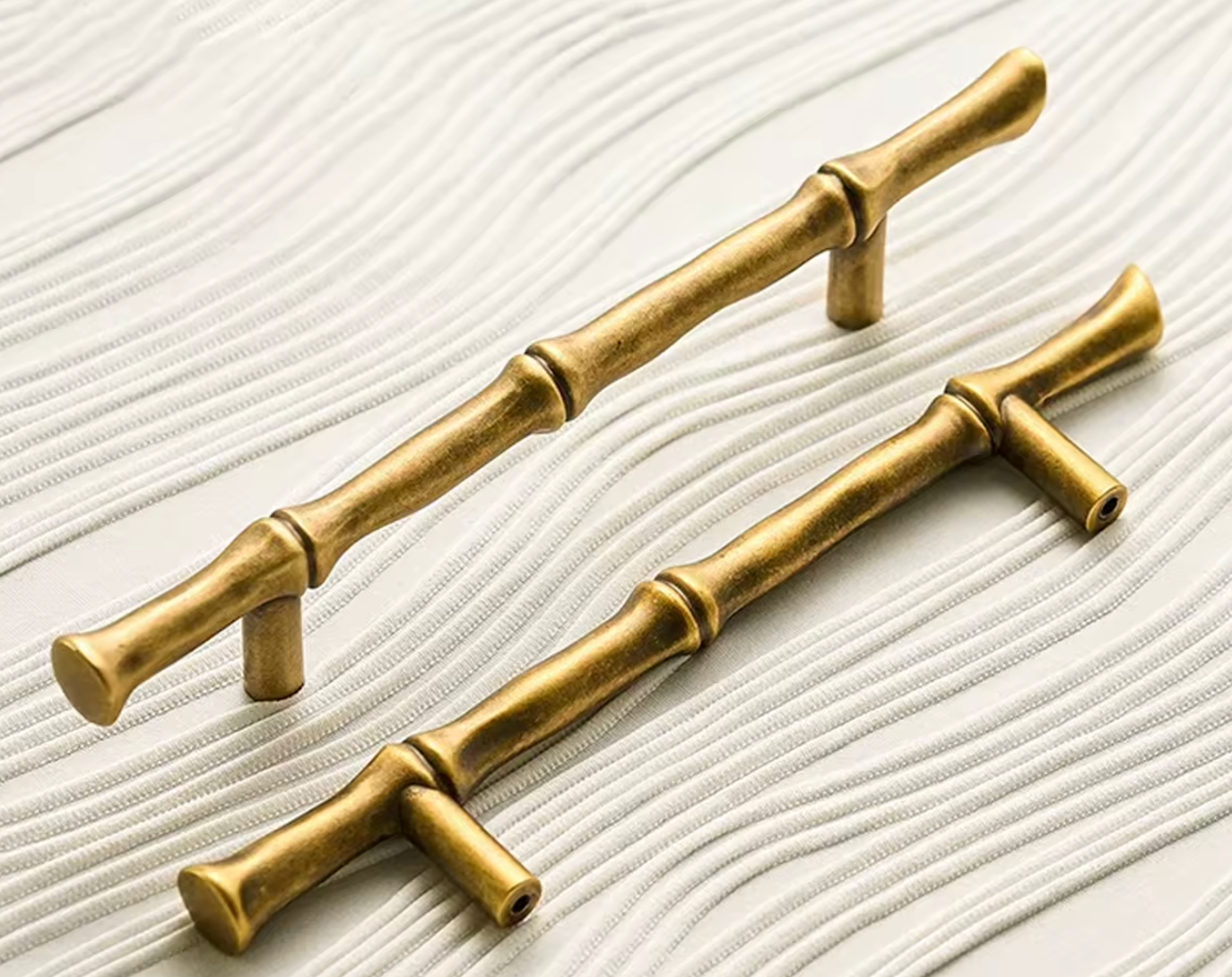 Two brass cabinet knobs with a bamboo joint design, displayed on a white textured background.