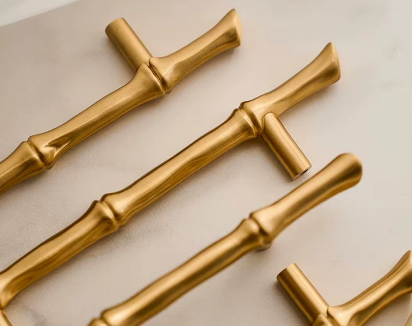 Gold bamboo-style cabinet handles arranged diagonally on a light beige surface.