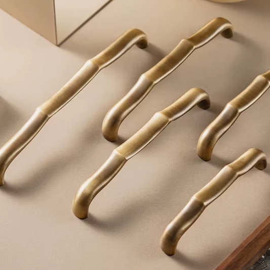Five curved cabinet handles in a brushed brass or gold finish, arranged diagonally on a warm beige surface.