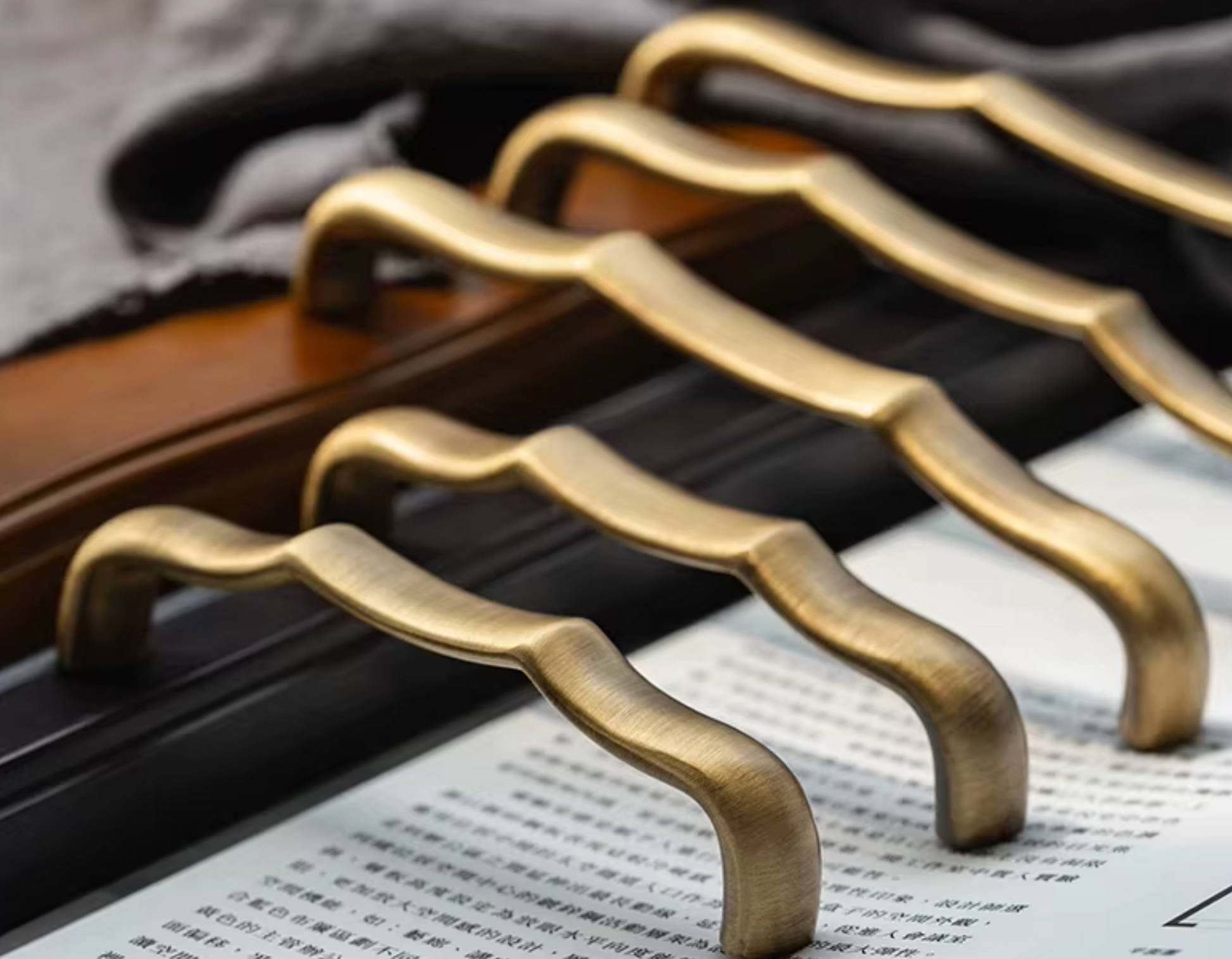 Five curved brass cabinet handles arranged diagonally on a dark wooden surface with printed papers underneath.