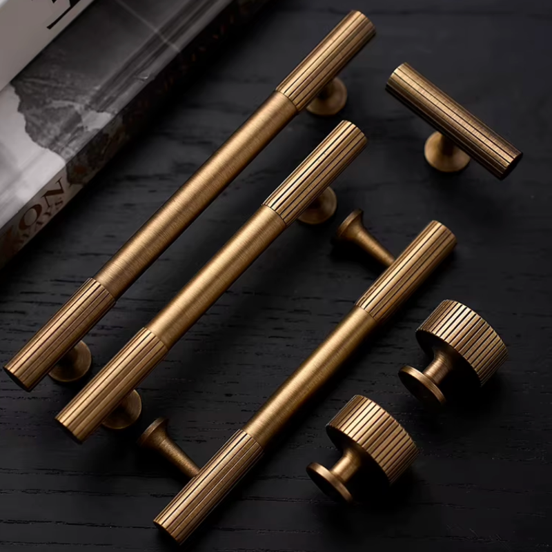 Six brass cabinet handles and knobs with a ribbed metallic finish, arranged on a dark textured wooden surface.