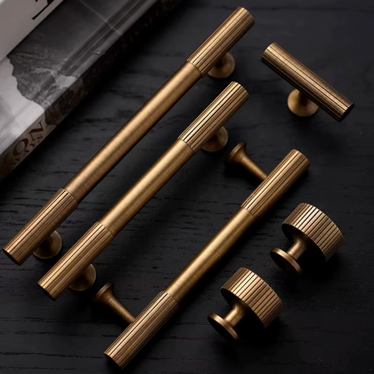 Six brass cabinet handles and knobs with a ribbed metallic finish, arranged on a dark textured wooden surface.