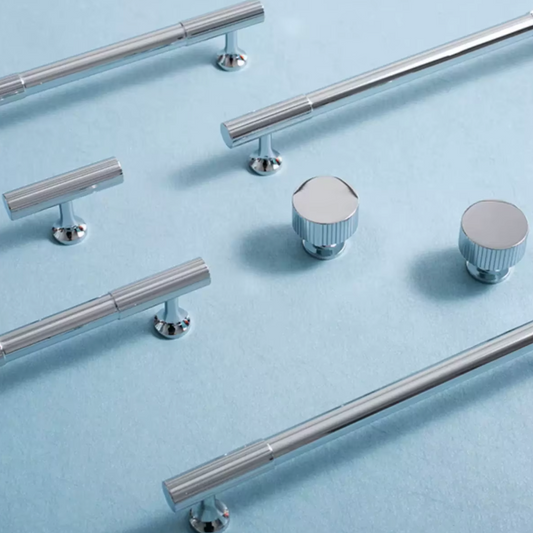 A set of polished silver cabinet hardware, including long bar pulls, round knobs, and smaller lever handles, arranged on a light blue textured background.