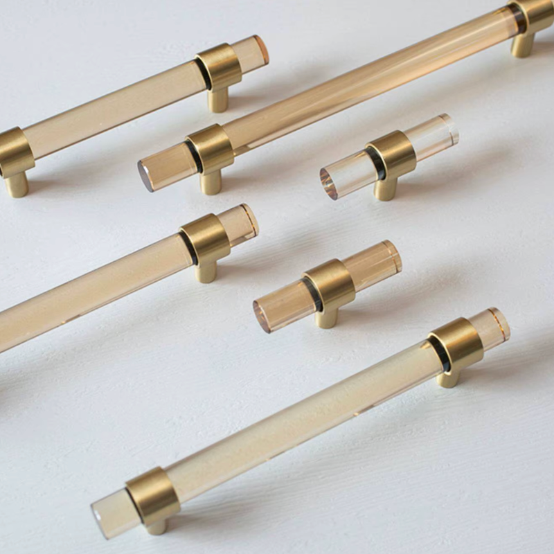 A set of modern cabinet handles with clear acrylic rods and brushed brass or gold-toned end caps and mounting bases, arranged on a clean white background.