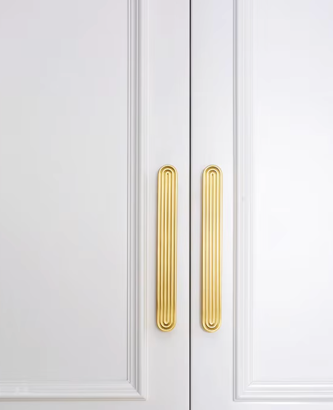 Two vertical gold cabinet handles mounted on white paneled double doors.