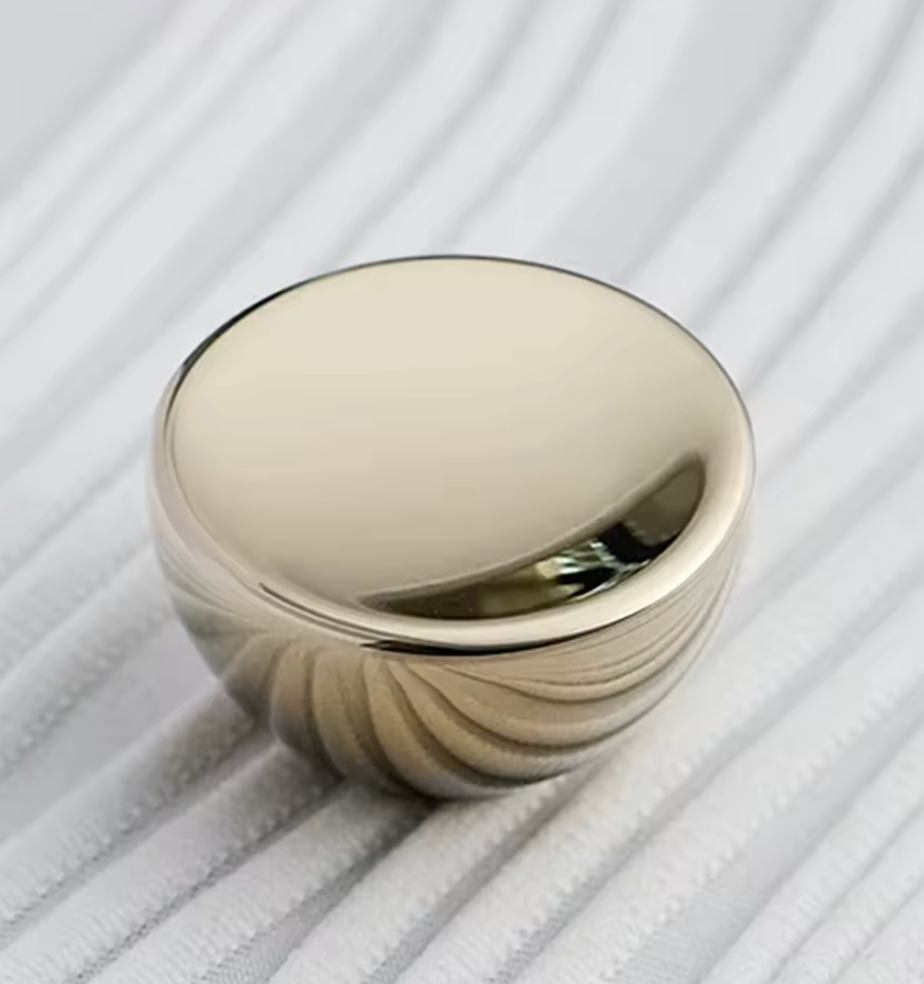 A polished metallic round knob or decorative cap with a reflective silver finish, resting on a white ribbed fabric surface.