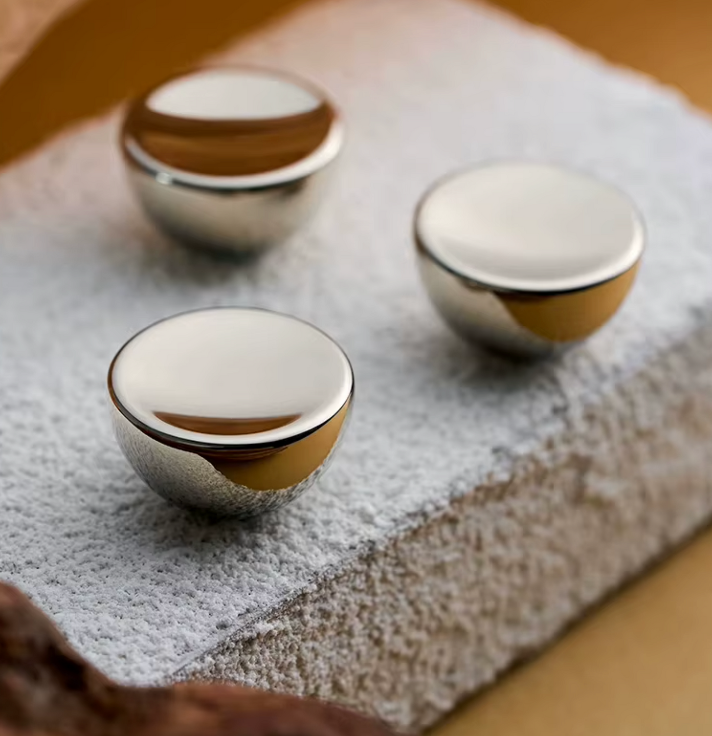 Three small round metallic knobs with a brushed silver finish and a polished gold edge, displayed on a textured light gray stone slab.