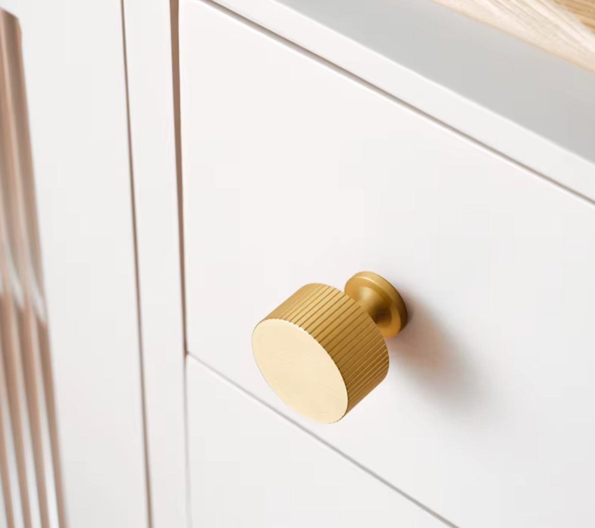 A close-up of a white cabinet or drawer featuring a round, ribbed brass knob.