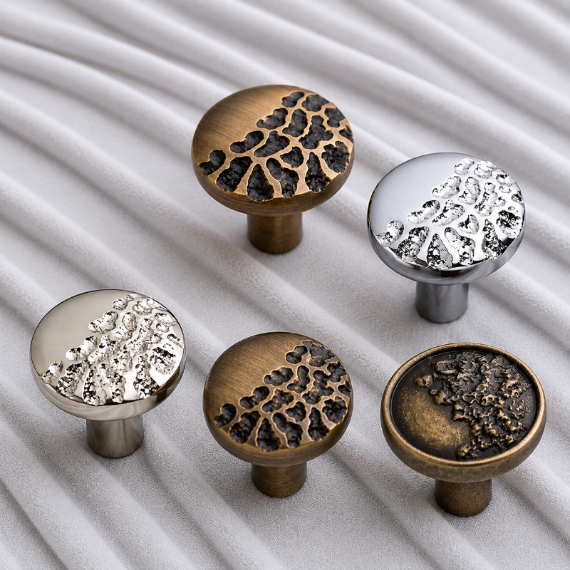 Five round cabinet knobs in antique bronze and polished silver finishes, arranged on a white textured fabric background.