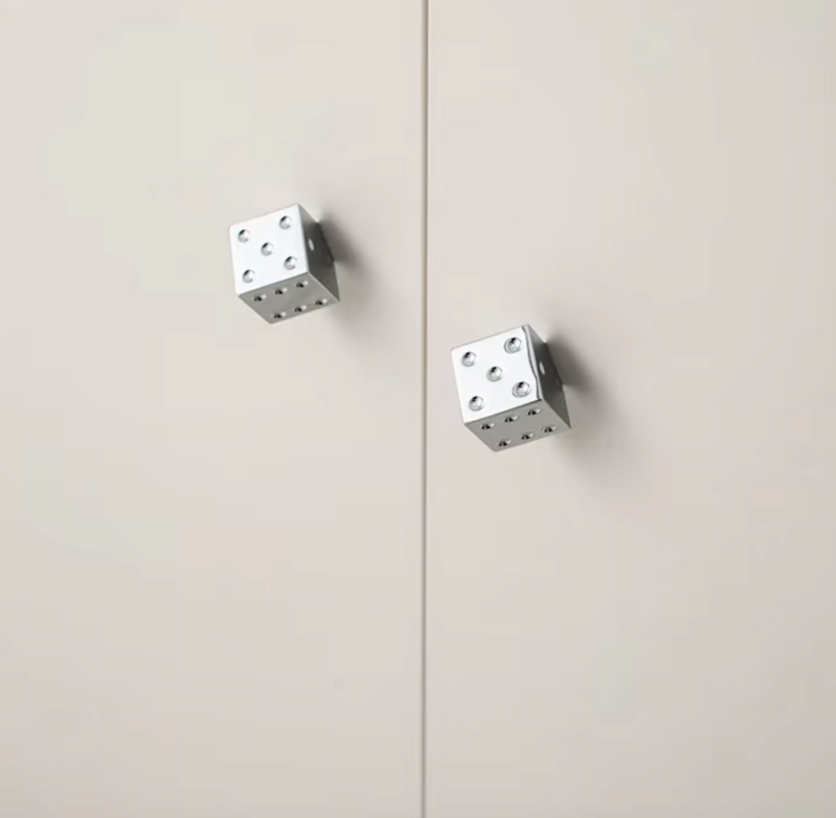 Two silver metal cube-shaped magnetic door stoppers mounted on a light beige door, with a vertical seam running down the center.