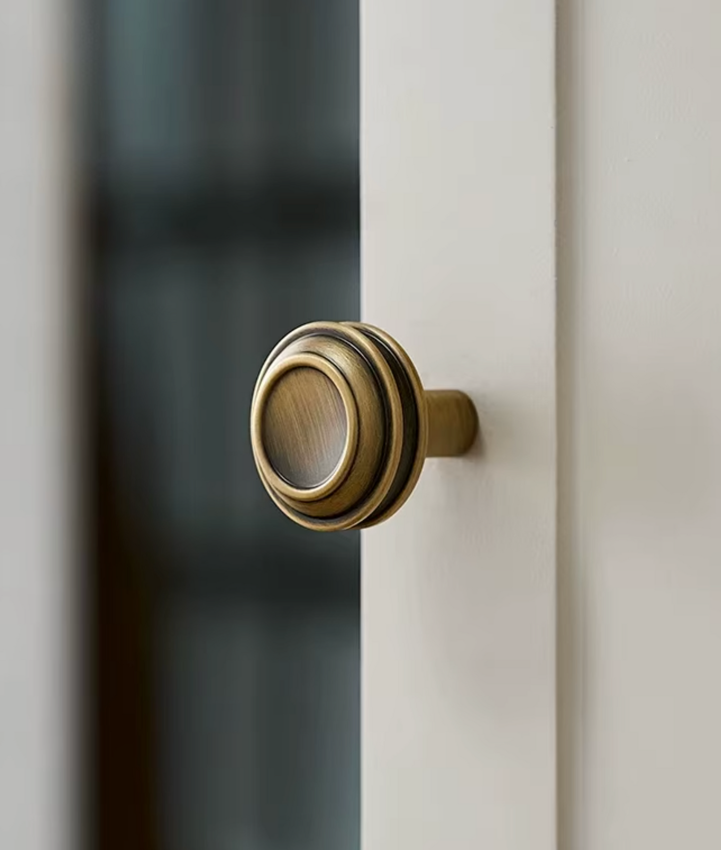 A close-up of a round, multi-tiered brass door knob mounted on a white door frame, with a softly blurred dark background.