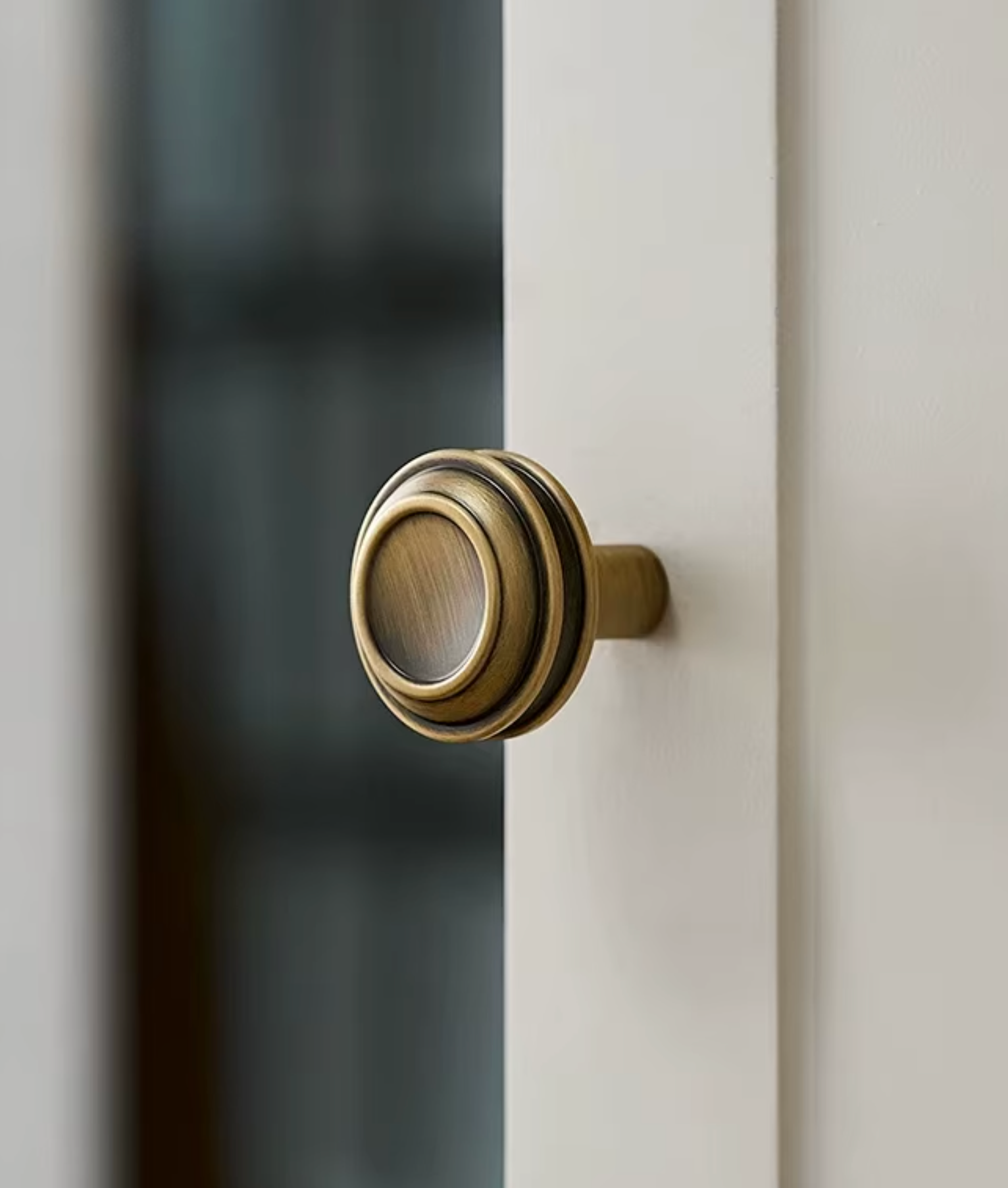 A close-up of a round, multi-tiered brass door knob mounted on a white door frame, with a softly blurred dark background.