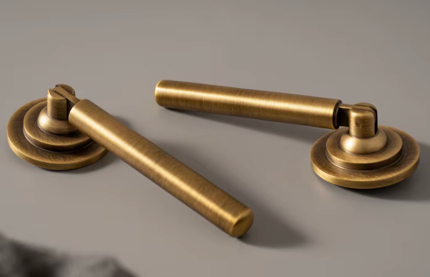 Two brass door handles with a brushed antique finish, displayed on a neutral gray background.