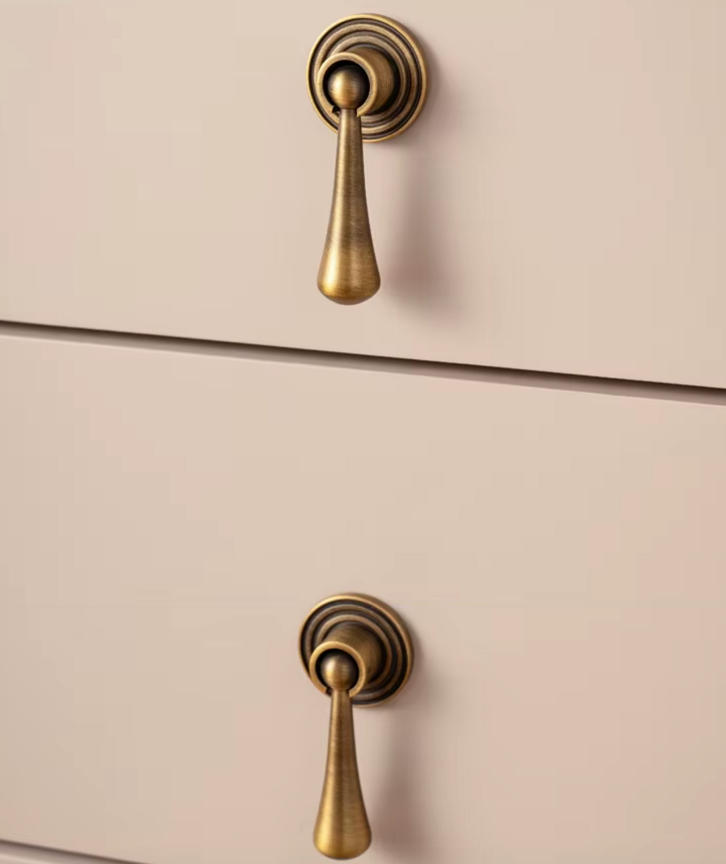 Two antique brass pull handles on a light beige wooden drawer front, shown in a close-up product shot.