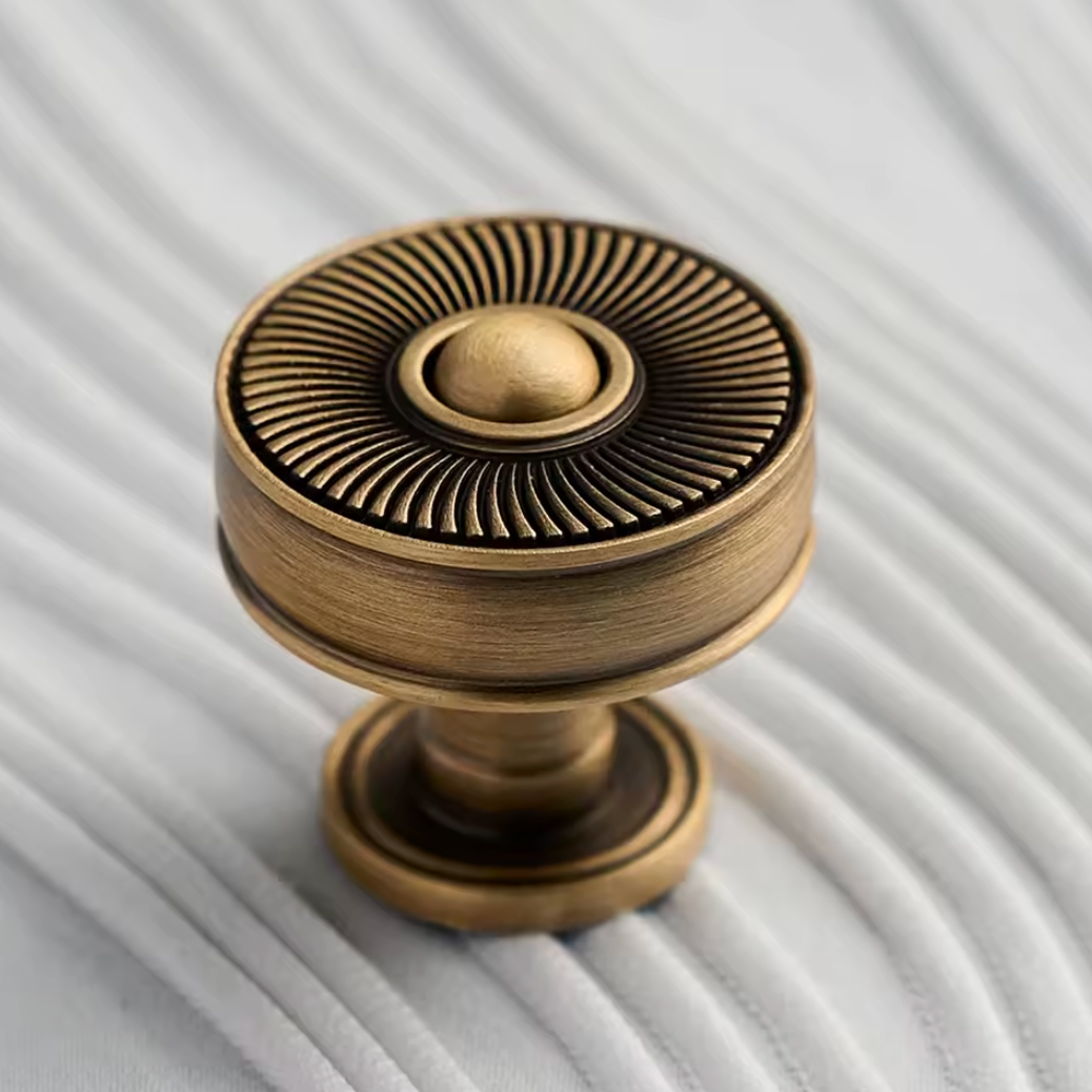 An antique bronze cabinet knob with a sunburst ribbed design, resting on a white textured fabric background.