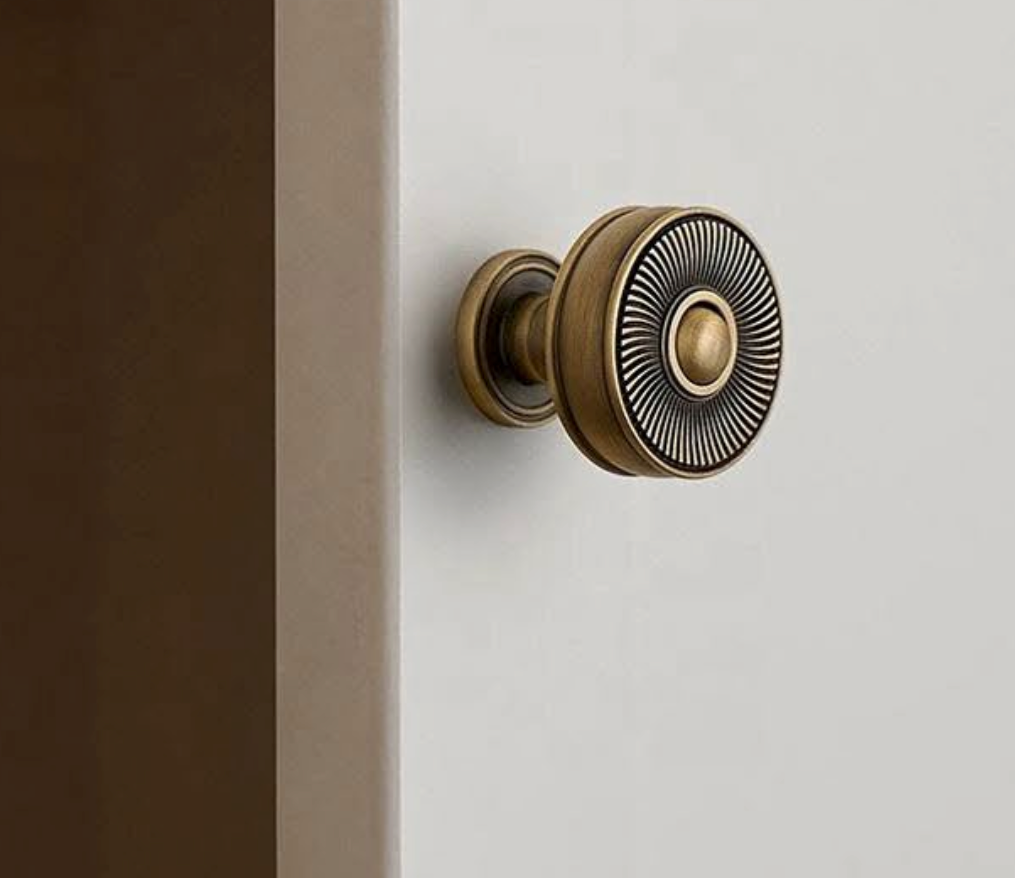A round antique bronze door knob with a textured sunburst pattern on the face, mounted on a white door next to a dark brown door frame.