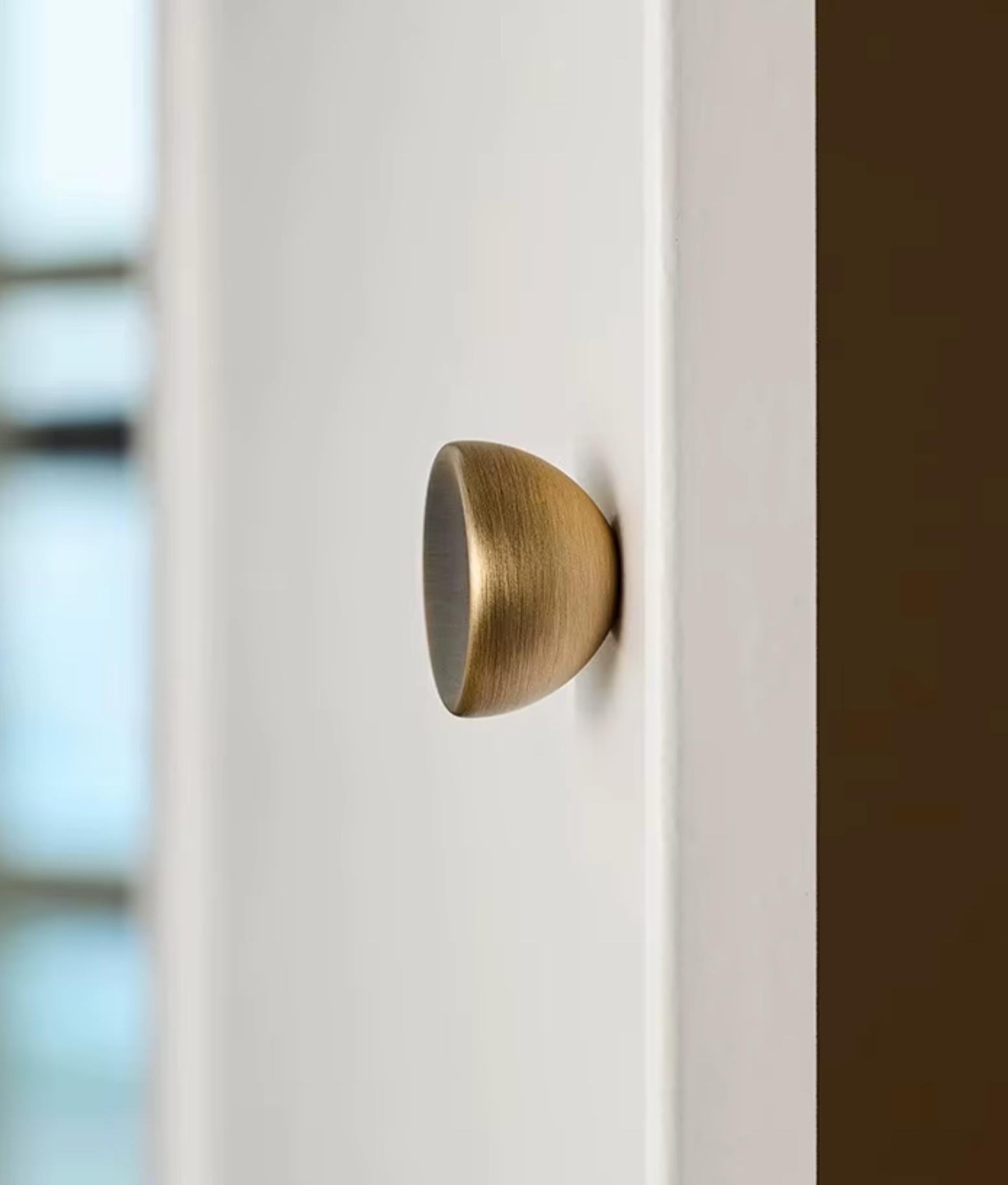 A close-up of a modern, dome-shaped door knob in a brushed brass finish mounted on a white door.