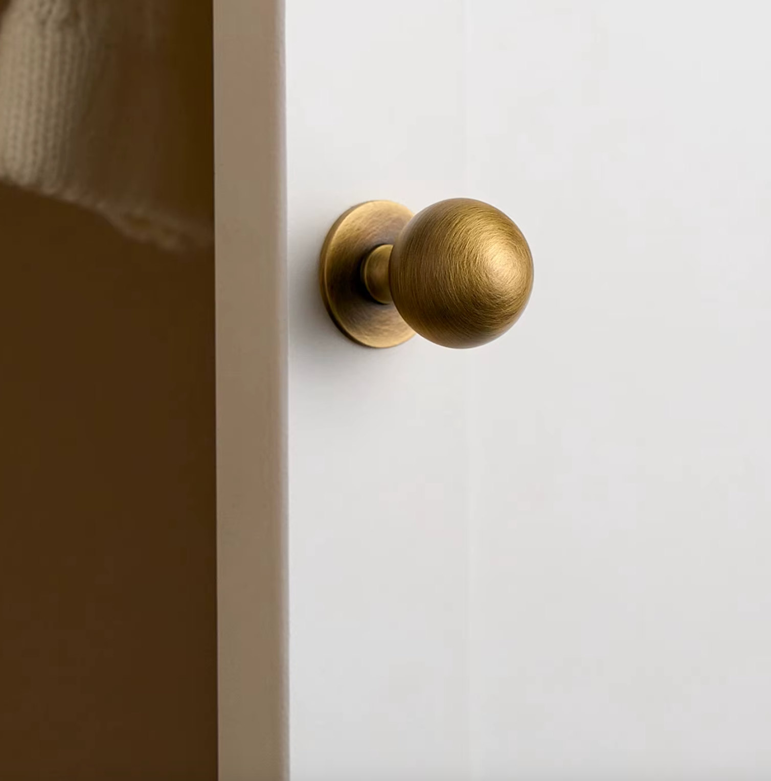 A round brass door knob with a brushed finish mounted on a white door next to a beige wall.