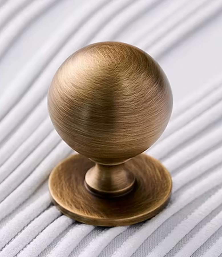 A round brushed brass cabinet knob with a matching round backplate, shown on a white ribbed surface.