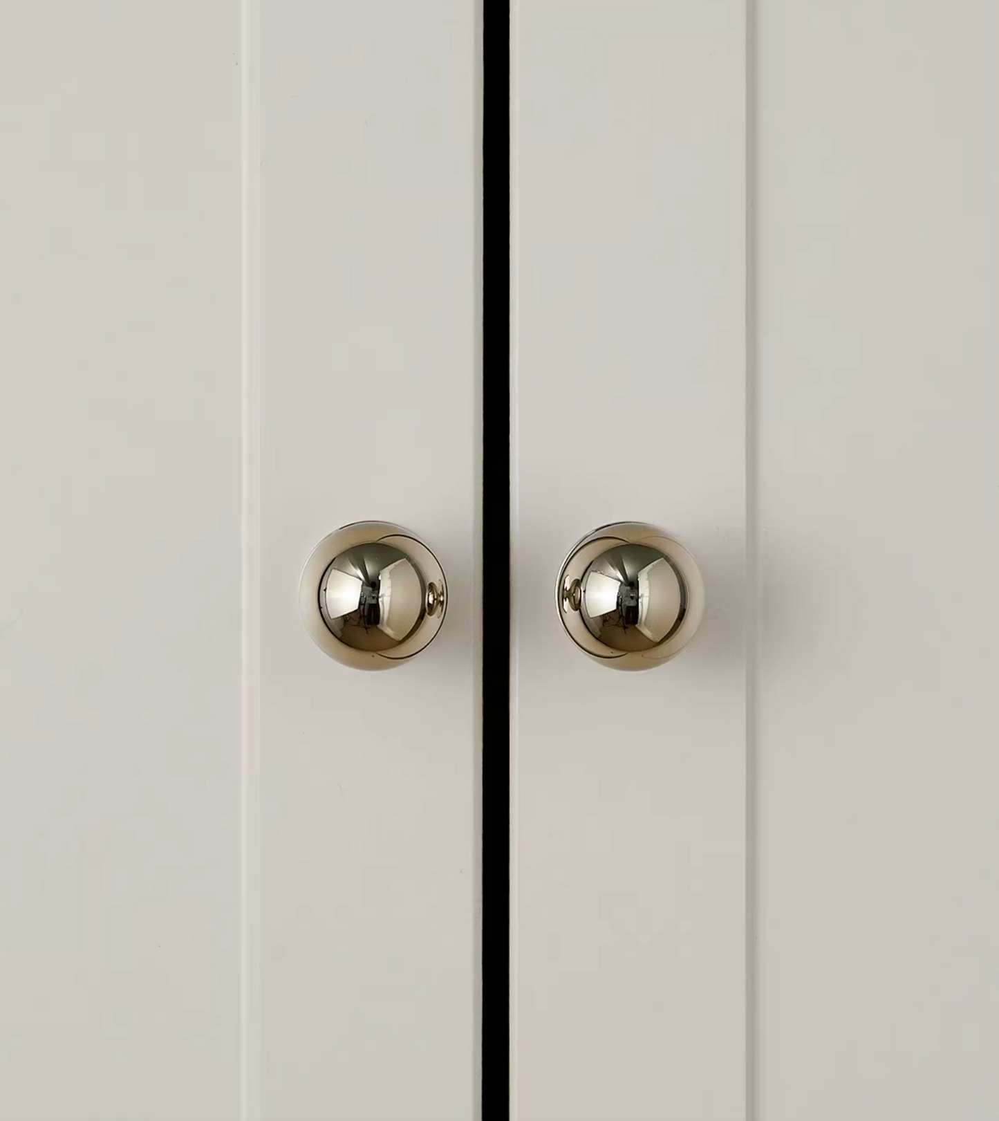 Two round polished silver cabinet knobs mounted on white paneled doors with a thin black vertical line between them.
