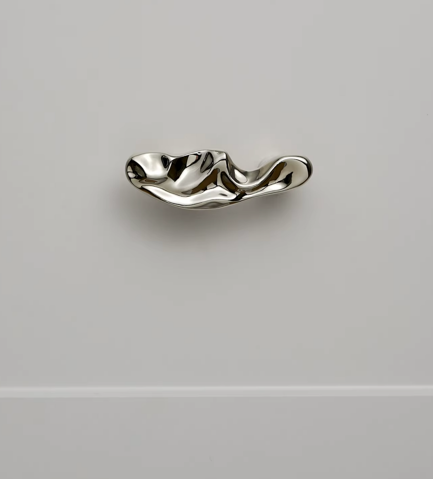 A polished silver wavy cabinet knob mounted on a light gray wall.