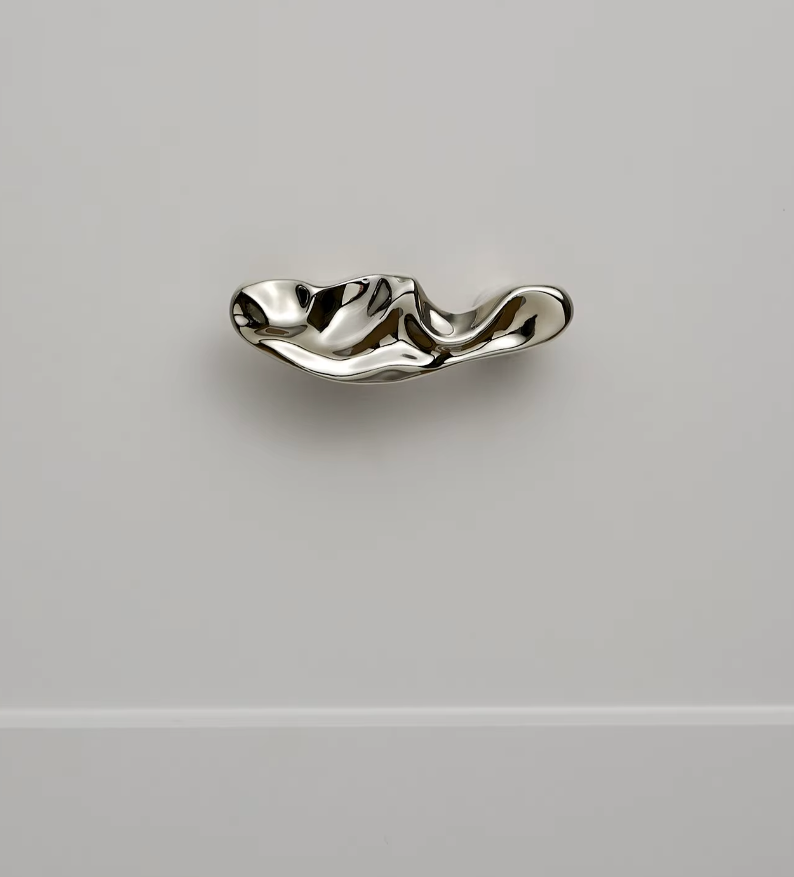 A polished silver wavy cabinet knob mounted on a light gray wall.