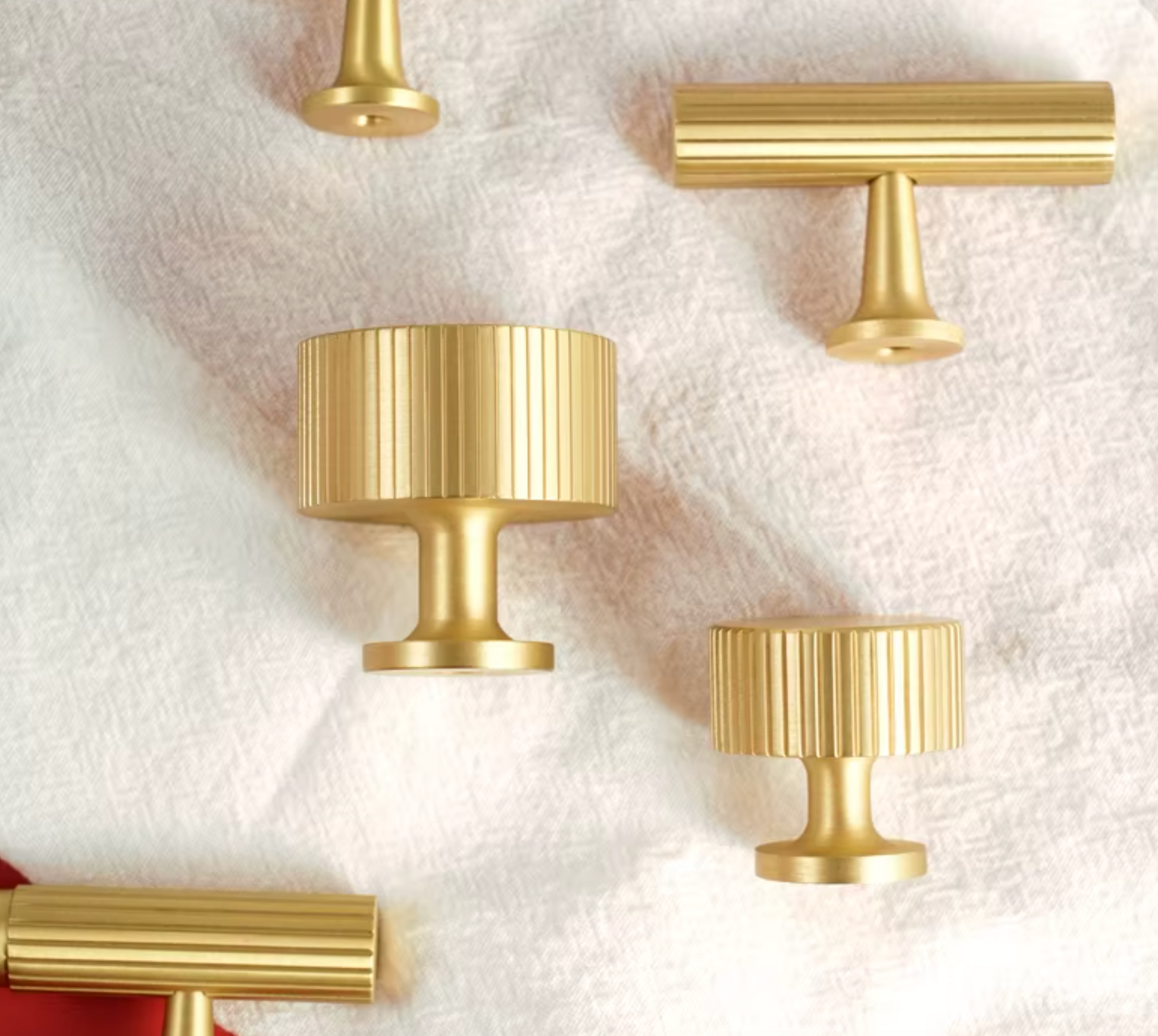 A set of brushed gold cabinet knobs with ribbed and cylindrical designs, arranged on a textured white fabric background.