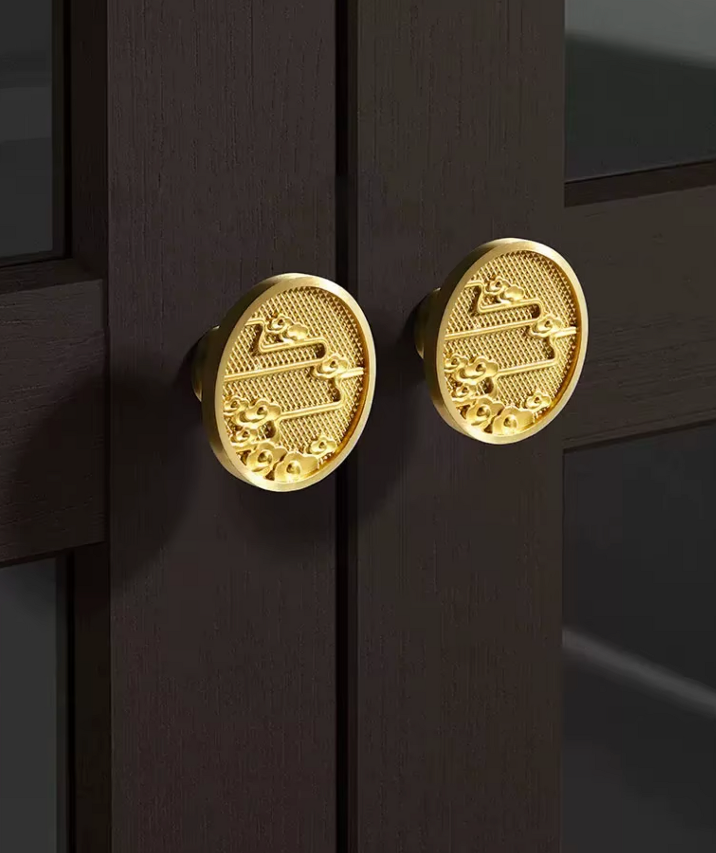 Two round gold-toned decorative cabinet knobs mounted on a dark wood door, shown in a close-up interior shot.