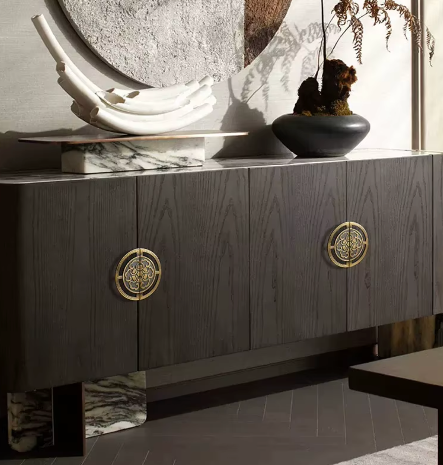 A modern dark wood sideboard or credenza with two round brass handles, styled in a contemporary interior setting with decorative objects on top.