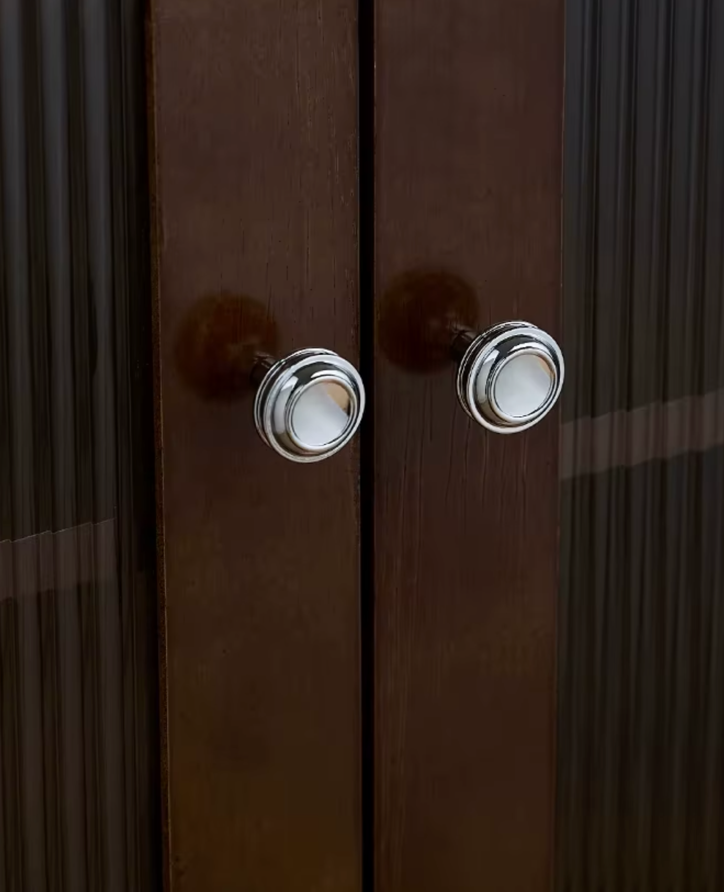 Two round polished silver metal door knobs mounted on dark brown wooden doors with vertical fluted glass panels.