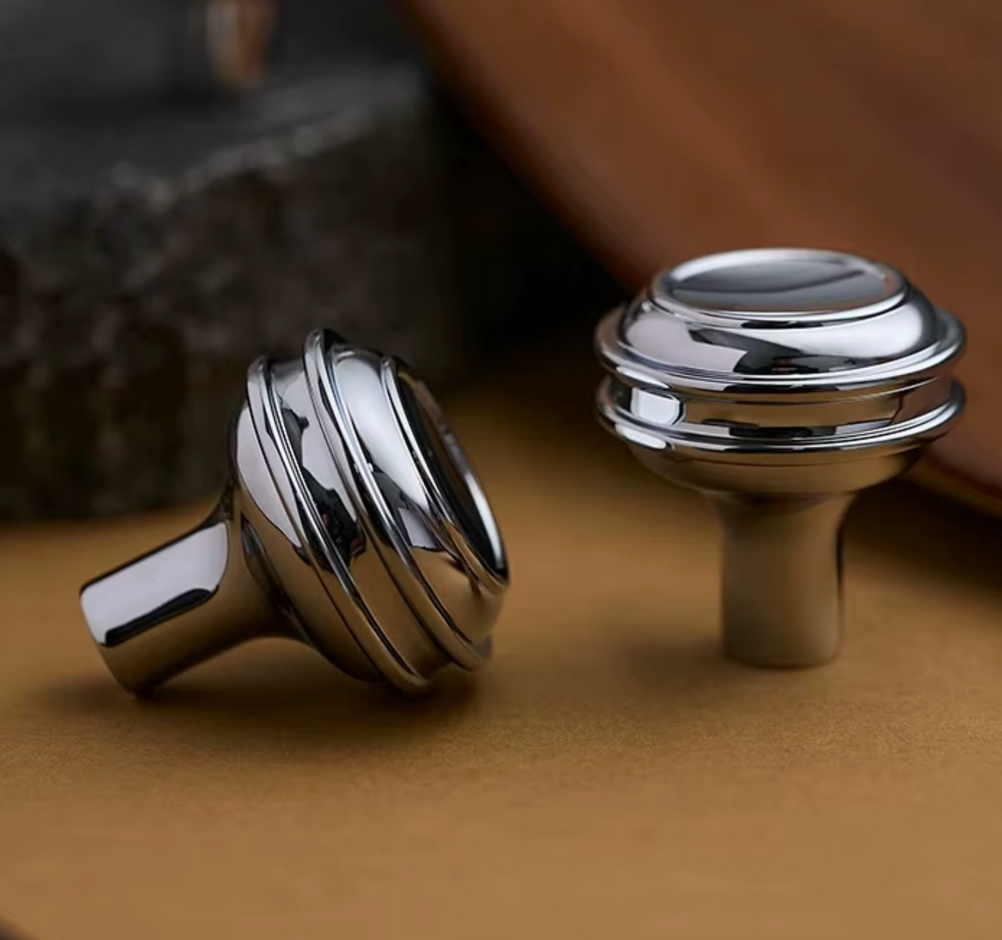 Two polished chrome cabinet knobs with a modern stacked-ring design, displayed on a textured brown surface.