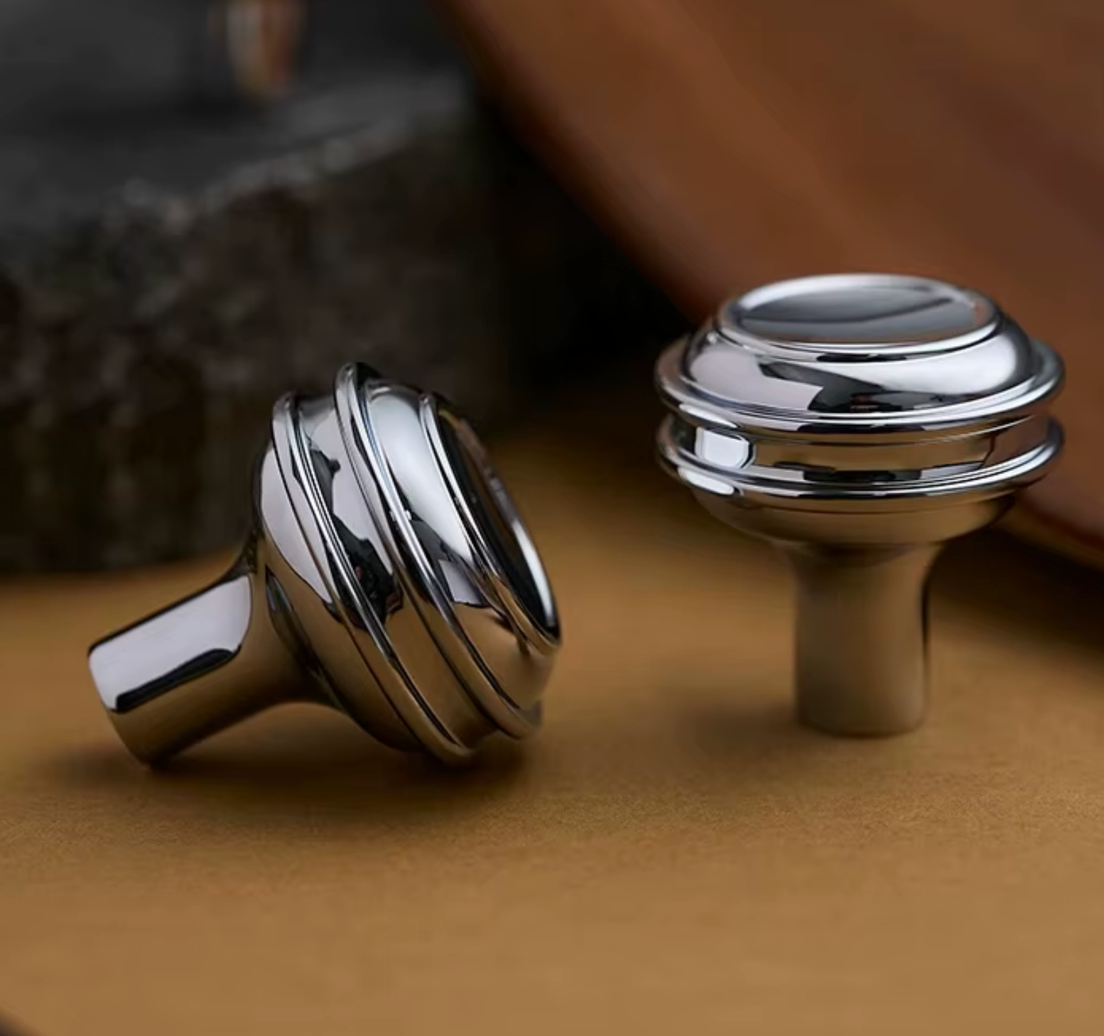 Two polished chrome cabinet knobs with a modern stacked-ring design, displayed on a textured brown surface.