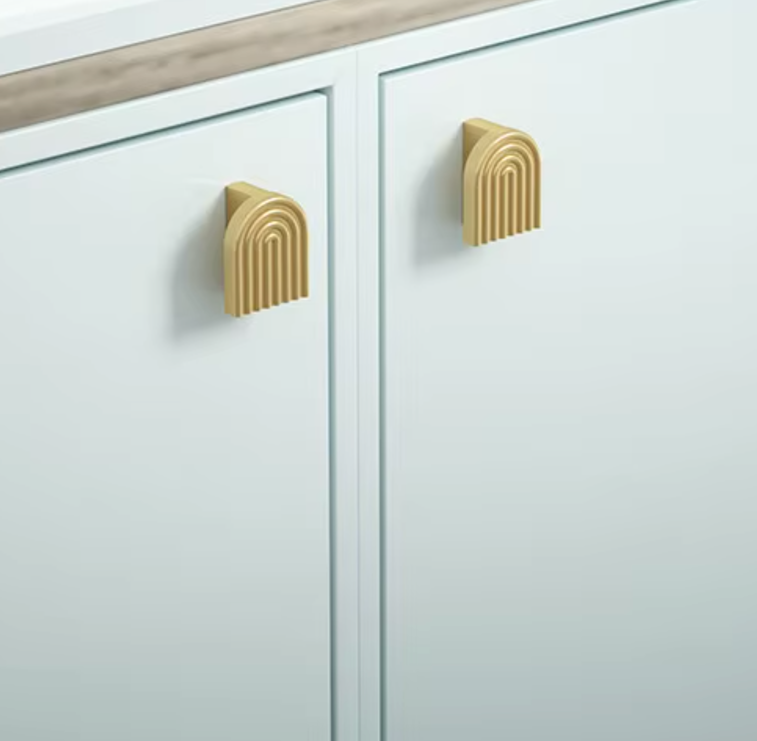 Six gold-toned cabinet knobs with a modern ribbed oval design, arranged diagonally on a white marble surface.