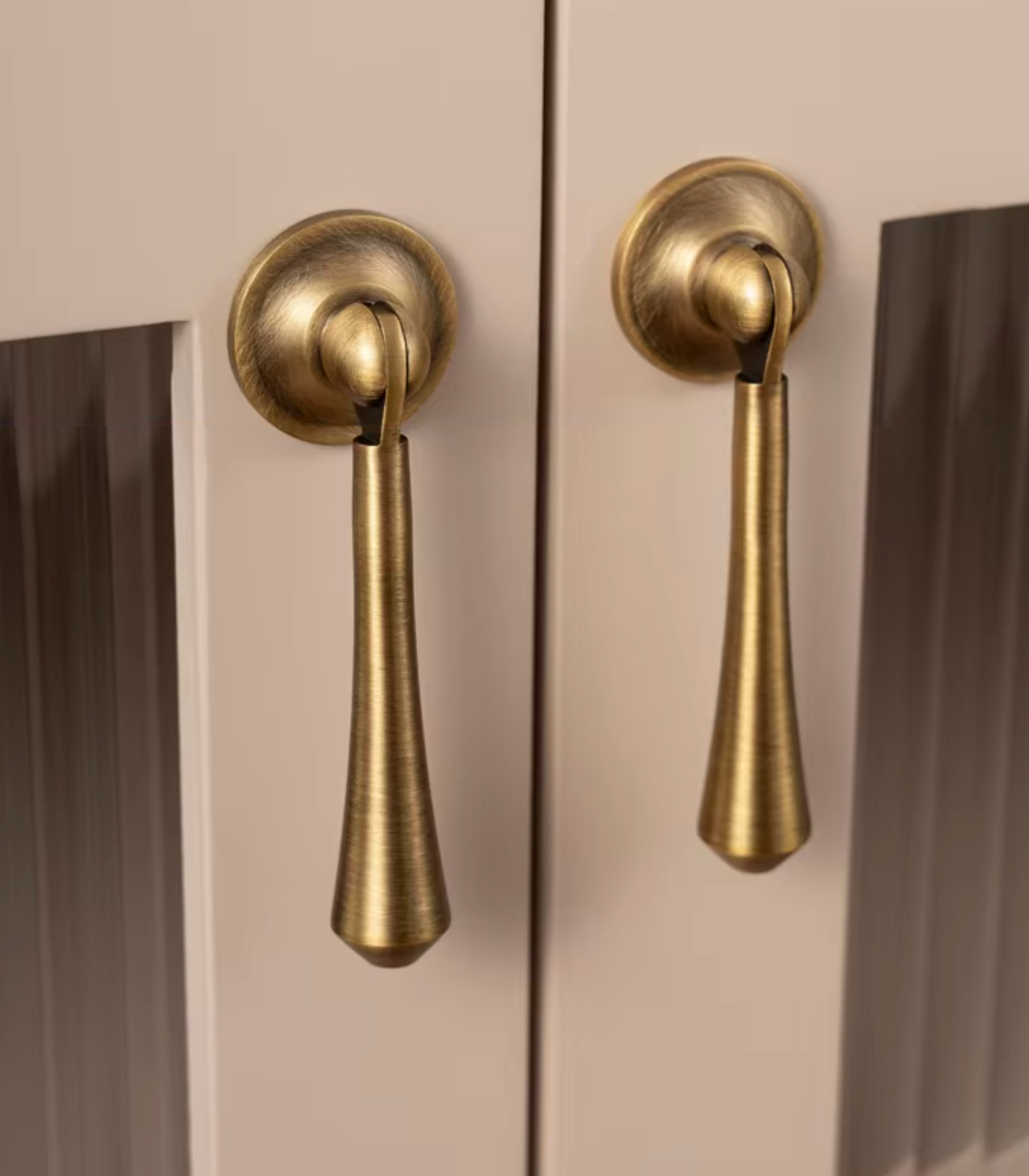 Two brass pull handles mounted on a cream-colored cabinet door, shown in a close-up view.