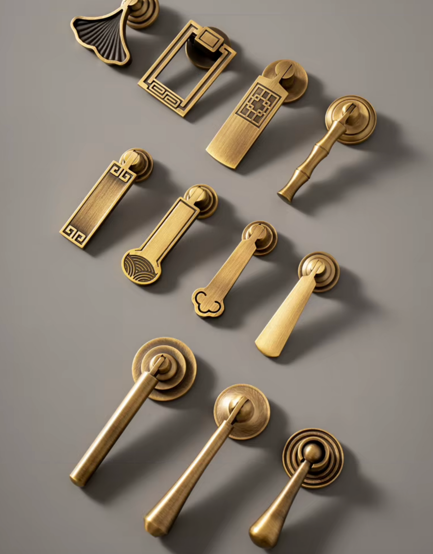 A set of ornate brass door pulls and drawer pulls arranged on a smooth gray surface, featuring traditional Chinese-inspired designs with geometric and floral details.