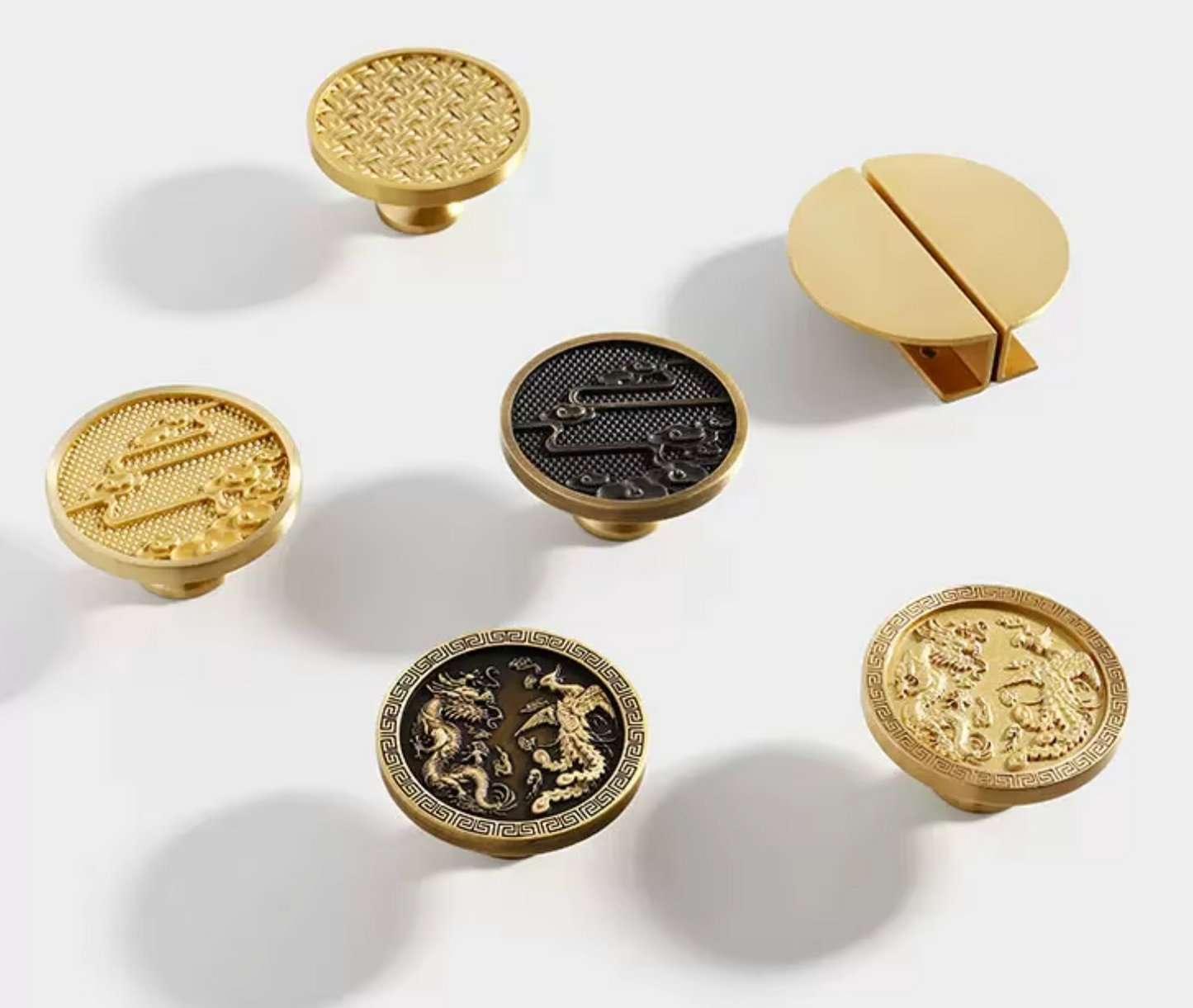 Six decorative cabinet knobs in a clean studio arrangement on a white background. Five knobs are round and metallic, with ornate embossed patterns in gold and black finishes, and one knob is shown open in a split-circle design.