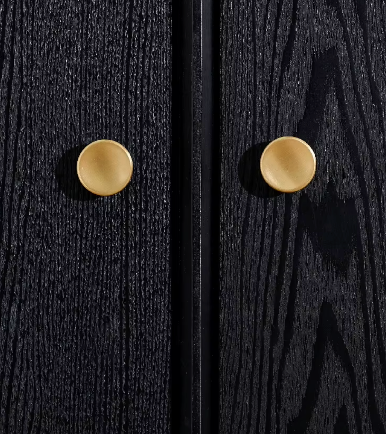 Two round, matte gold cabinet knobs mounted on a textured black wood door, shown in a close-up split view.