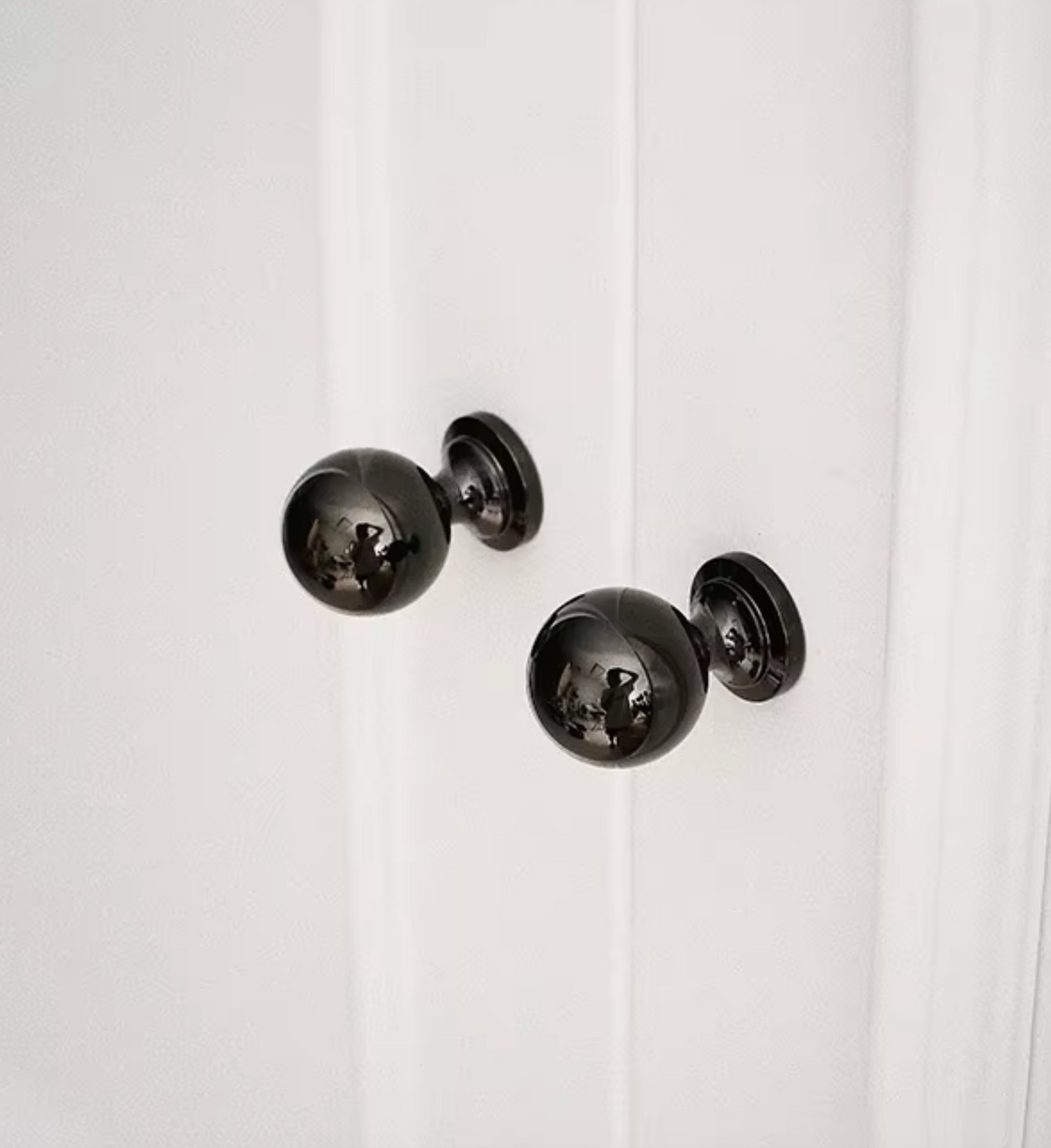 Two glossy black spherical door knobs mounted on a white paneled door.