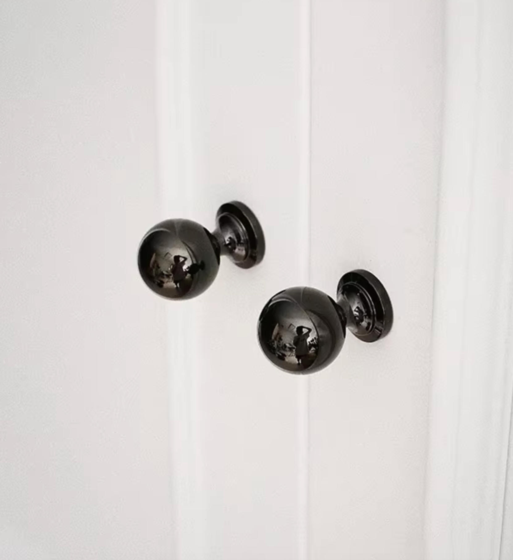 Two glossy black spherical door knobs mounted on a white paneled door.